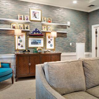 A cozy living room with a sofa, armchair, and a wooden cabinet adorned with pictures and lamps.