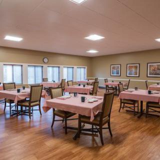 A quiet dining room with neatly arranged tables and chairs, featuring wooden flooring and wall artwork.