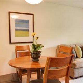 A cozy dining area featuring a wooden table with two chairs, decorated with a potted plant and wall art.