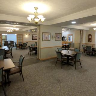 A spacious dining room with multiple tables and chairs, decorated with chandeliers and wall art.