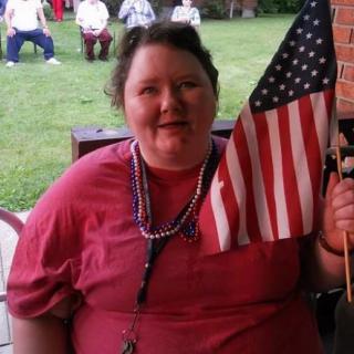 A person holding an American flag outdoors, likely celebrating a patriotic event.