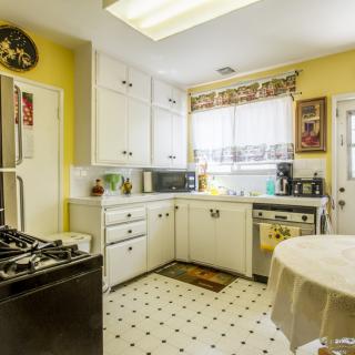 A cozy kitchen with bright yellow walls and white cabinetry, featuring various appliances and a patterned floor.