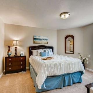 A cozy bedroom featuring a neatly made bed, a bedside lamp, and tasteful decor including a mirror and painting.
