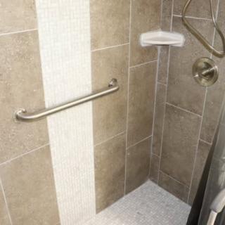 A tiled shower with a grab bar and showerhead.
