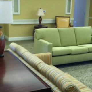 A cozy living room featuring a green sofa, a striped couch, and a wooden coffee table, with warm yellow walls and decorative lamps.