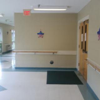 A view of a well-lit corridor featuring beige walls, a green mat, and accessible handrails.