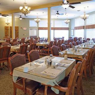 A spacious dining room with neatly arranged tables and chairs, illuminated by chandeliers.