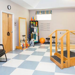 A well-equipped therapy room featuring a wooden ramp, exercise equipment, and an orange exercise ball.
