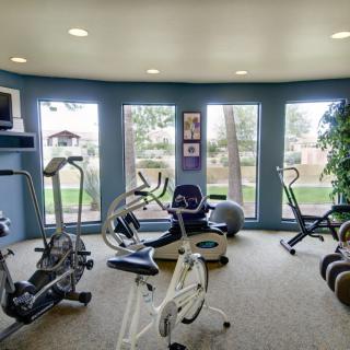 A well-lit gym with various exercise equipment and large windows.