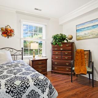 A cozy bedroom with a window, bed, and wooden furniture, featuring decorative art and a warm atmosphere.