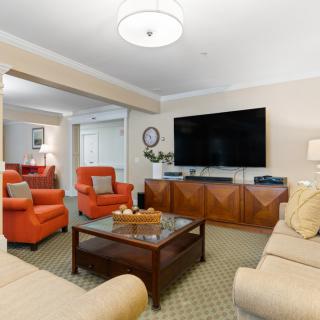 A cozy living room featuring orange armchairs, a large flat-screen TV, and a wooden coffee table.
