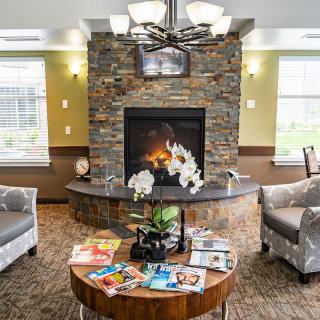 A cozy living room featuring a stone fireplace, comfortable armchairs, and a coffee table with magazines and decorative plants.