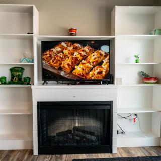 A cozy living room setup with a fireplace, shelves, and a TV displaying delicious food.