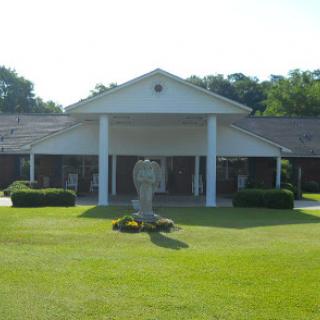 A serene view of a building surrounded by neatly trimmed grass and a statue in the foreground.