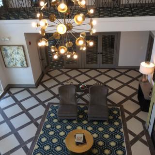 A stylish and modern lobby area with a central chandelier, decorative floor pattern, and contemporary furniture.