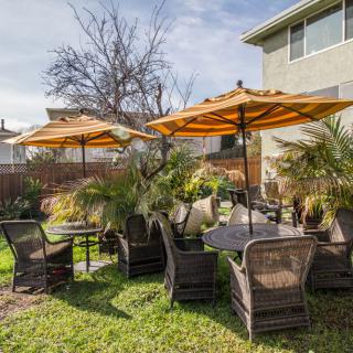 A cozy outdoor patio setup with tables, wicker chairs, and orange umbrellas on a grassy lawn.
