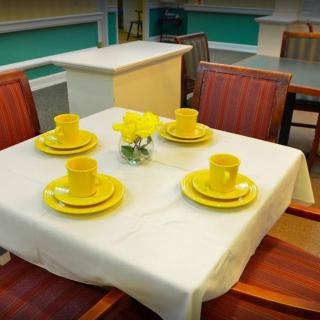 A neatly arranged dining table with vibrant yellow dishes and cups, set on a white tablecloth.