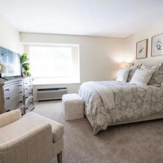 A cozy and elegantly furnished bedroom with a large bed, dresser, and natural light from a window.