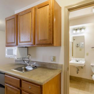 A small kitchen area with wooden cabinets, a sink, and a view into an adjacent bathroom.