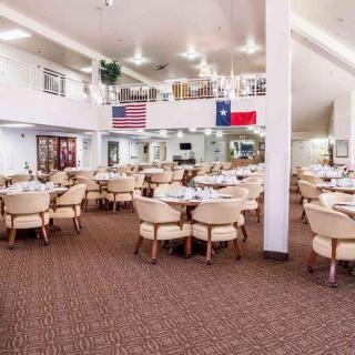 A spacious restaurant dining area with neatly arranged tables and chairs, featuring American and Texas flags on the wall.