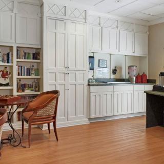 A cozy kitchen area with white cabinets, bookshelves, and wooden flooring.