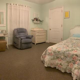 A cozy bedroom with floral bedding, a comfortable chair, and a dresser.