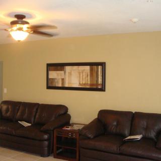 A cozy living room with dark leather sofas, a ceiling fan, and a framed painting on the wall.