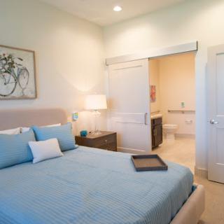 A serene and modern bedroom featuring blue bedding and minimalist decor, with a view of an adjoining bathroom.