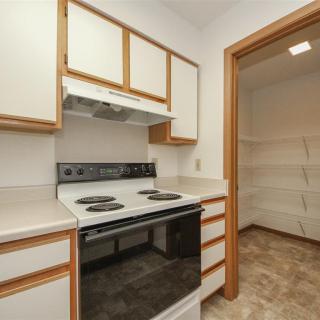 A compact kitchen featuring a stove and oven, with ample cabinetry and an adjacent pantry.