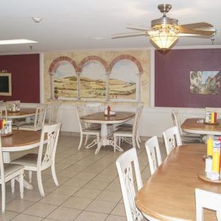 An empty restaurant dining area with neatly arranged tables and chairs, decorated with wall art and a ceiling fan.