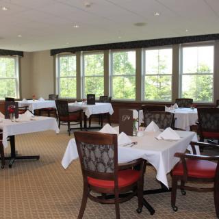 A neatly arranged dining area with tables and chairs, featuring natural light from the large windows.