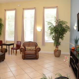 A cozy living room with large windows, tiled flooring, and decorative plants.