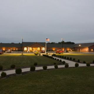 An illuminated building at dusk with a pathway and flagpole in front.