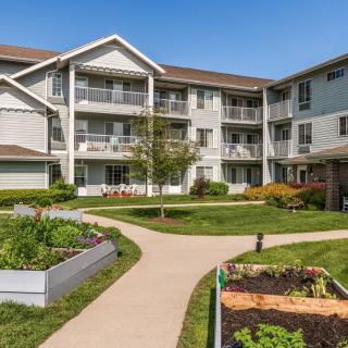 A modern apartment building featuring balconies and a well-maintained garden with raised plant beds along a winding pathway.