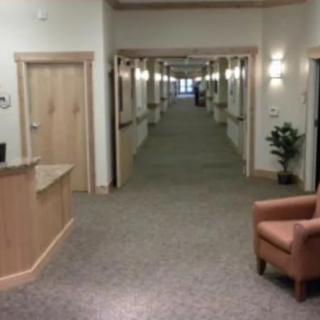 A long carpeted hallway with doors on each side, featuring a reception desk and an armchair.