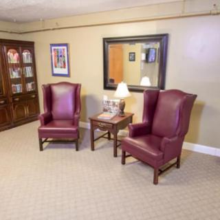 A cozy waiting area with two leather chairs, a small table with a lamp, and a large mirror on the wall.