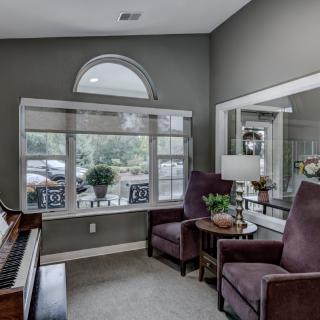 A cozy living room with a grand piano, comfortable chairs, and natural light from the large window.