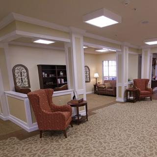 A cozy lounge area with armchairs, shelves, and decorative elements in a well-lit interior space.