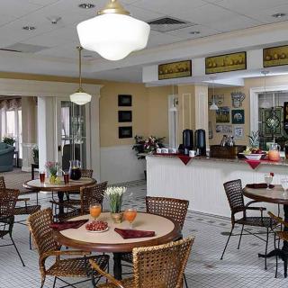 A cozy dining area featuring several round tables with wicker chairs, soft lighting, and a counter for service in the background.