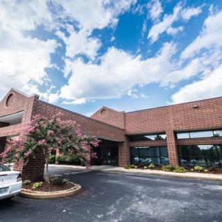 A commercial brick building with a parking lot and trees under a partly cloudy sky.