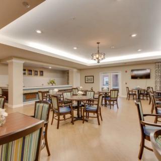 A well-lit dining area with neatly arranged tables and chairs, featuring a central chandelier and modern decor.