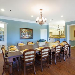 A spacious dining room with a long table and chairs, featuring blue walls and a chandelier.