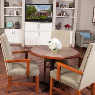 A cozy dining area featuring a round table and two chairs, with shelves and a television in the background.