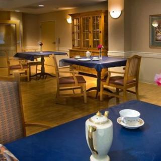 A cozy dining area with tables and chairs, set with tablecloths and a teapot on the foreground table.