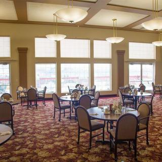 An elegant dining room with tables and chairs arranged on a patterned carpet, featuring large windows that let in natural light.