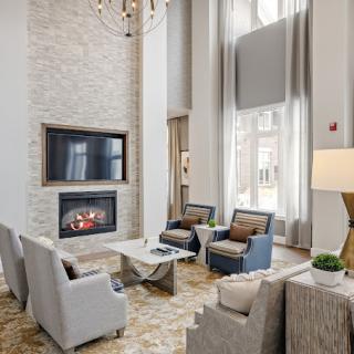 A modern living room with a fireplace and comfortable seating area, featuring high ceilings and ample natural light.