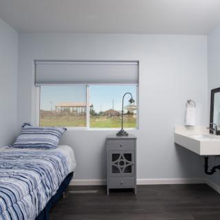 A cozy and modern bedroom featuring a twin bed, minimalist nightstand, and a large window with a view.