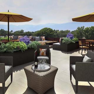 A cozy outdoor patio with comfortable seating, umbrellas for shade, and lush greenery.