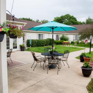 A tranquil courtyard with a patio set under a blue umbrella, surrounded by greenery and potted plants.