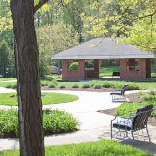 A peaceful park with benches, a gazebo, and a winding pathway surrounded by lush greenery.